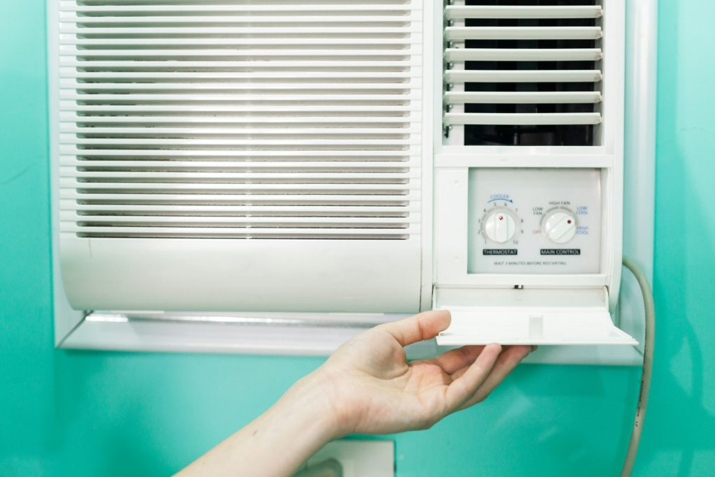 A person carefully adjusts the settings on a wall-mounted air conditioning unit, wondering, "Why is my air conditioner leaking water?