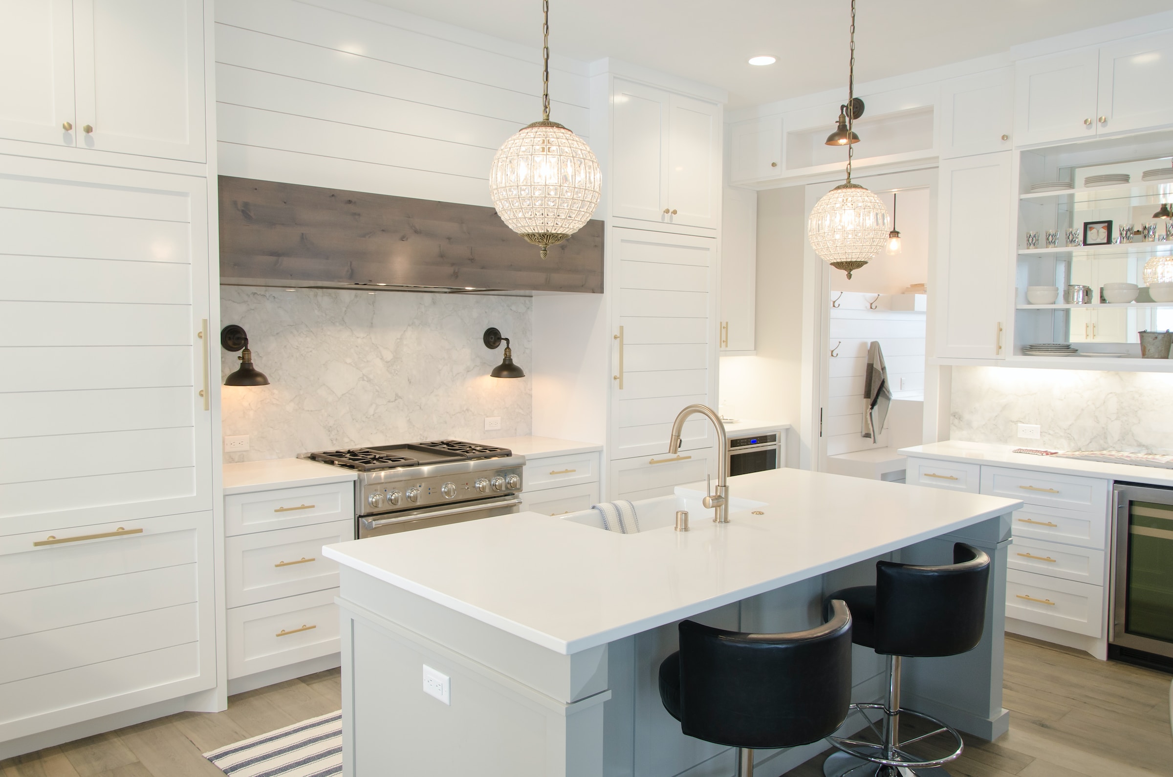 A kitchen with white cabinets and bar stools, featuring modern lighting.